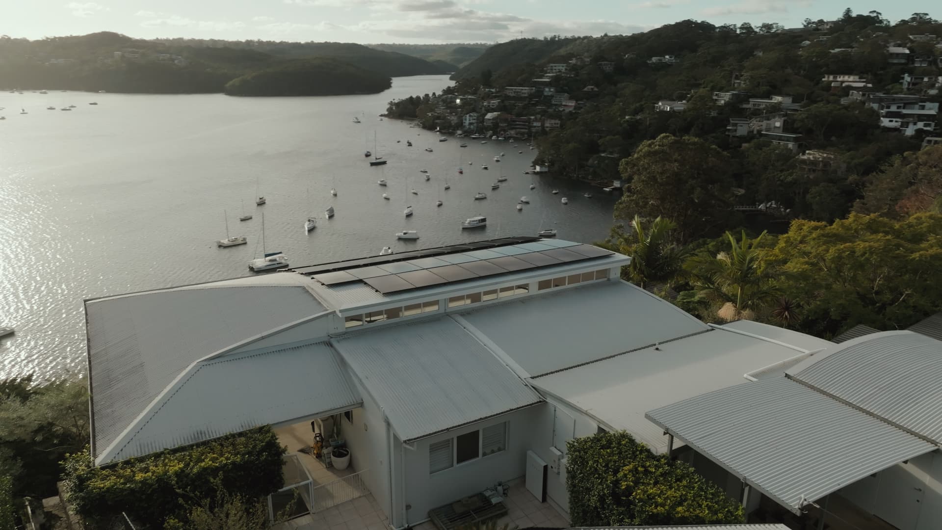 Aerial view of a waterfront home with black rooftop solar panels overlooking a bay of moored yachts